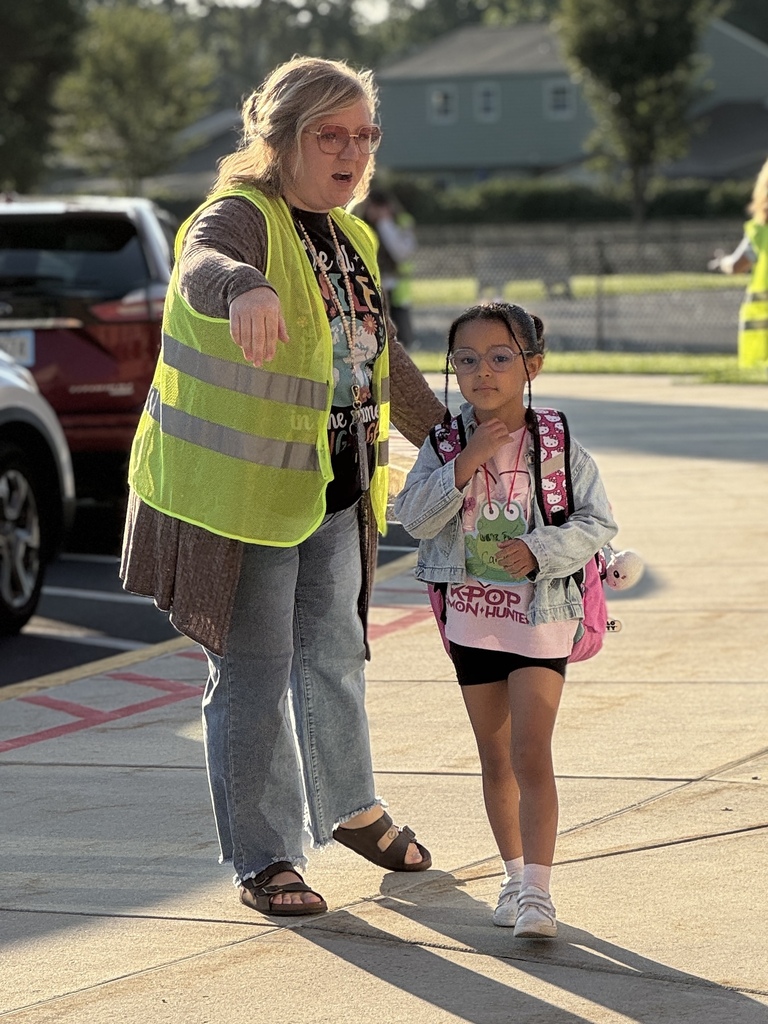 A staff member wearing a bright yellow vest greets a student at the start of a school day.