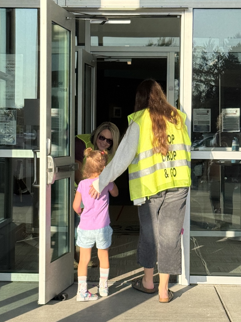 Staff with yellow stop group and go vests help a student into a school.