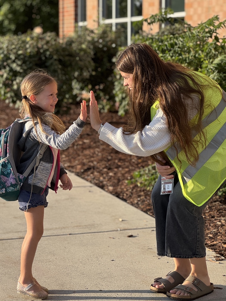 A staff member in a bright yellow vest gives a high five to a student.