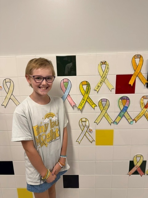 A young girl stands next to a wall decorated with yellow ribbons.