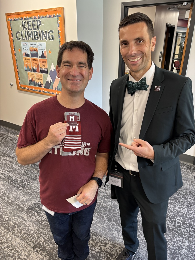 A man in a suit presents a pair of branded socks to a colleague.