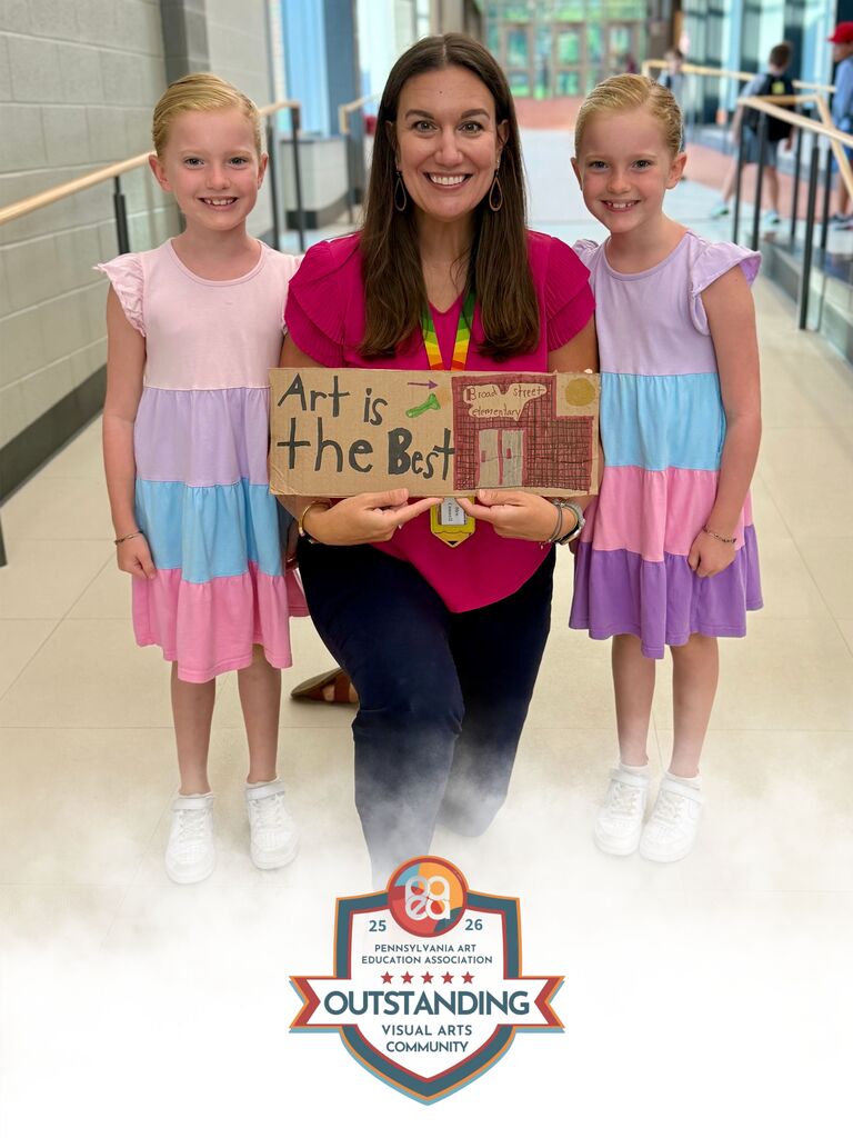 Two girls give an adult a hand-drawn "art is the best" sign.