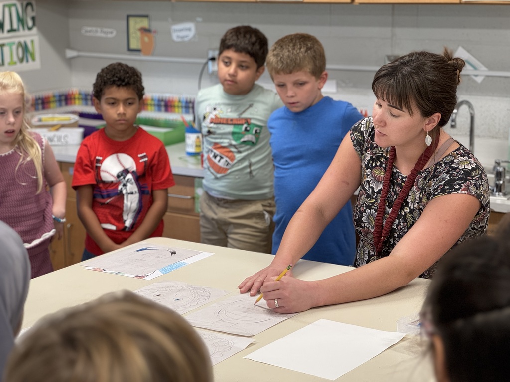 A teacher is surrounded by students as she leads an art lesson.