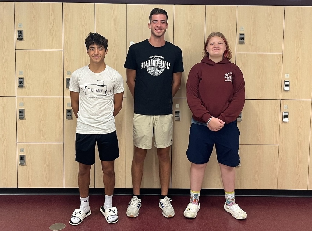 Three students stand in front of lockers in a school hallway.