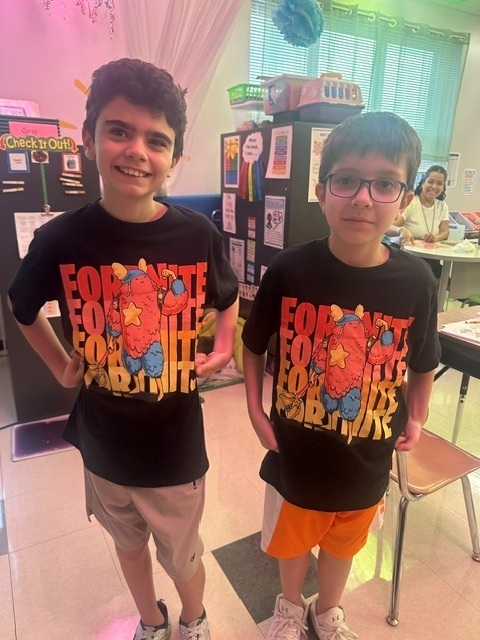 Two boys stand in a classroom wearing matching Fortnite tshirts.