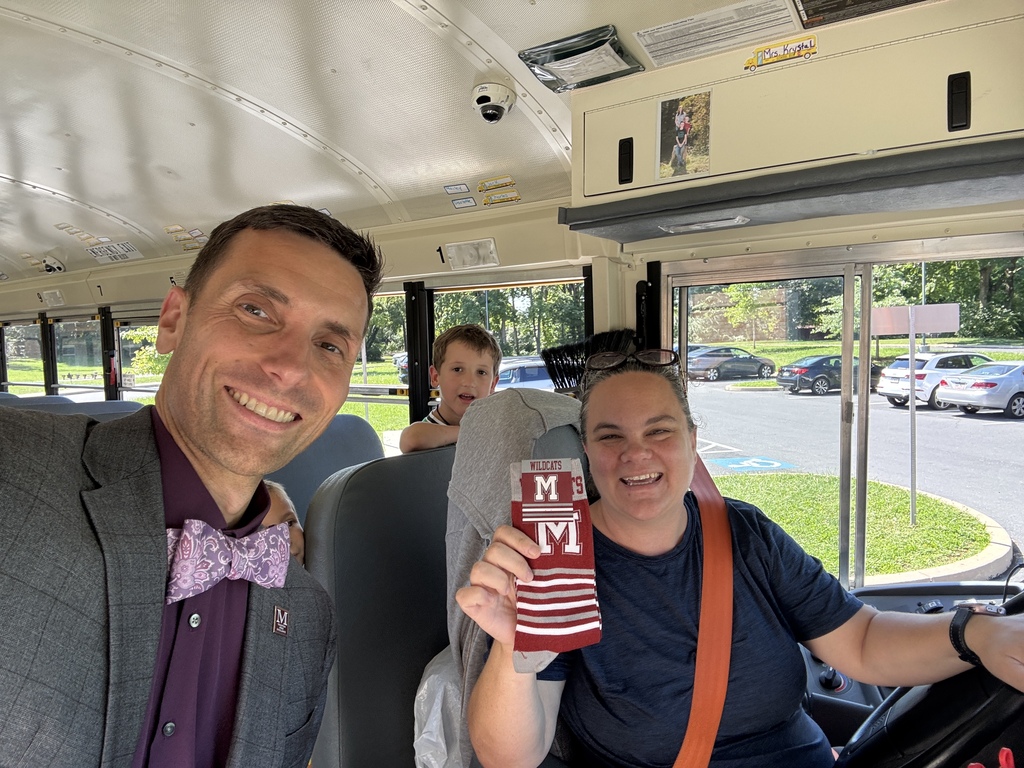 A man hops aboard a school bus to present a bus driver with a pair of branded socks with a young student pops up just in time to sneak into the background of the photo.