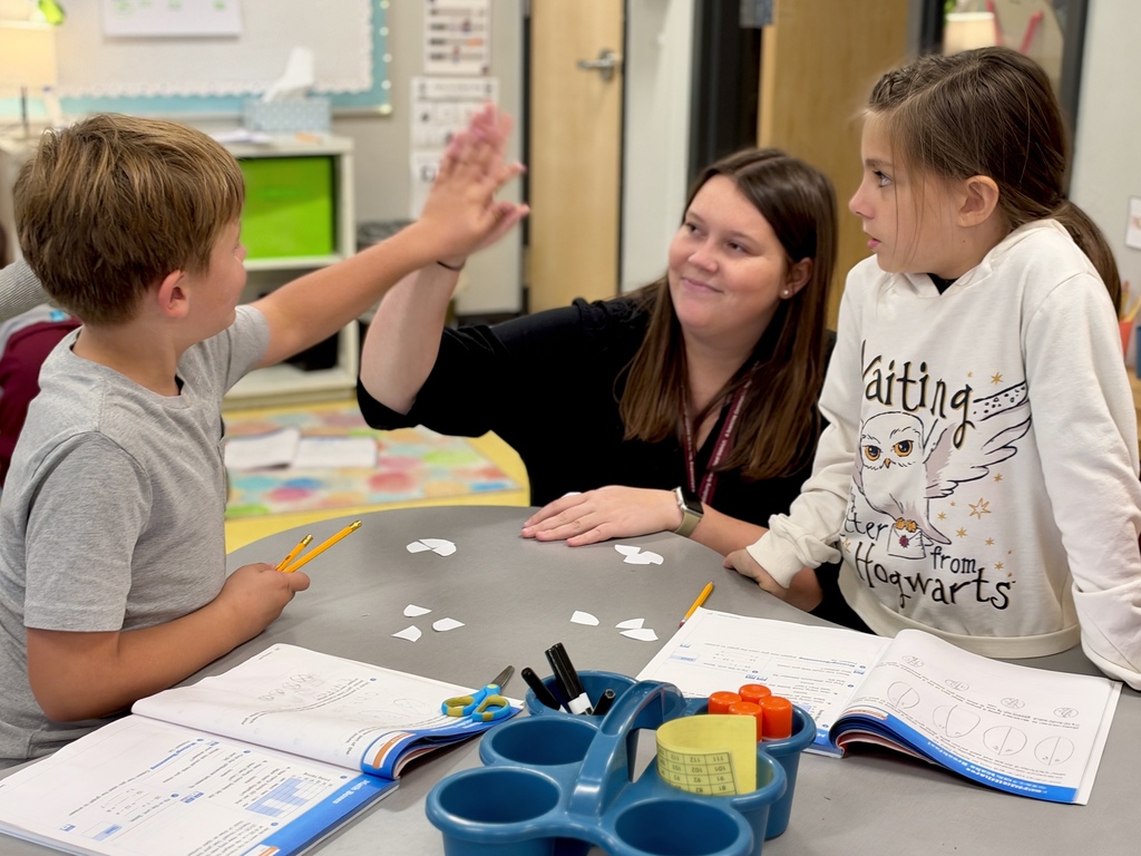 A student gets a high five from a teacher after successfully working on a math assignment.
