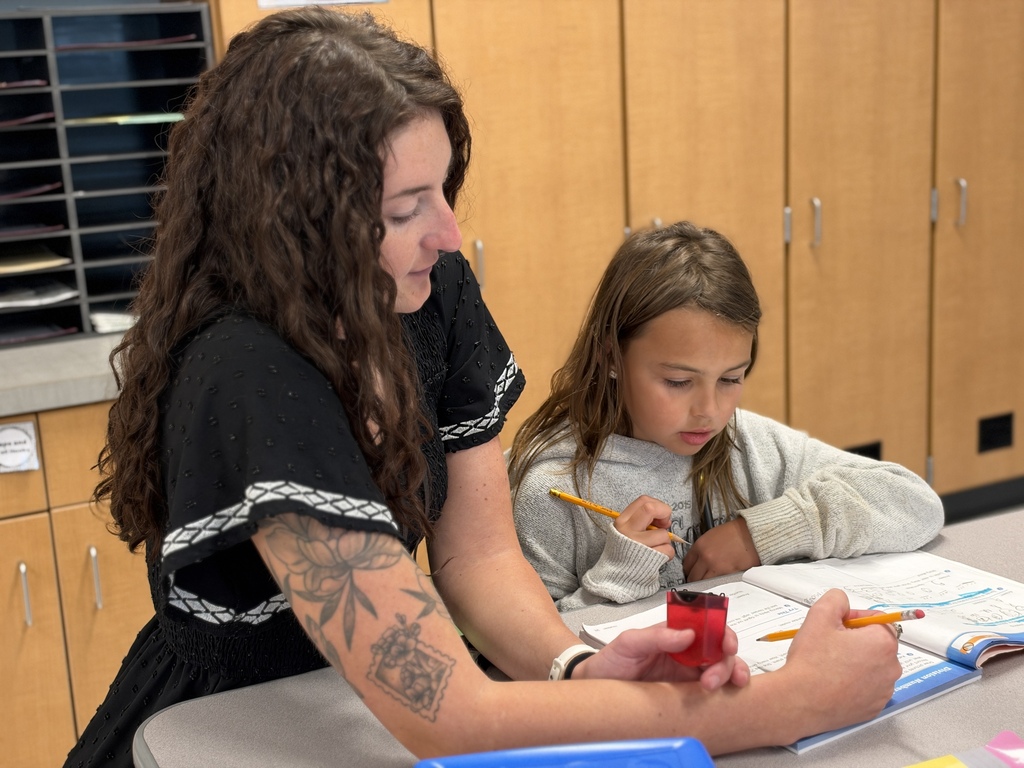 A teacher helps a student with a math assignment in a classroom.