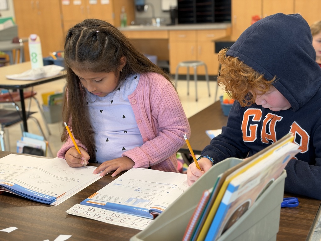 Two students work on a math assignment at a classroom table.