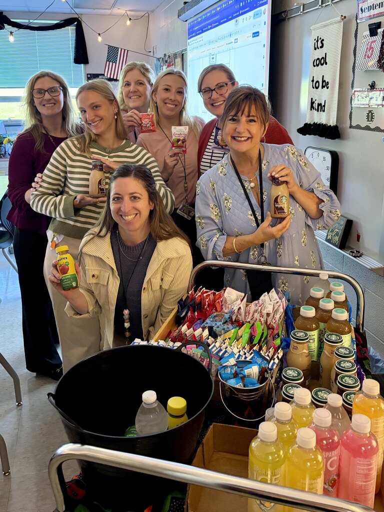 Teachers stand behind a snack cart in a classroom.