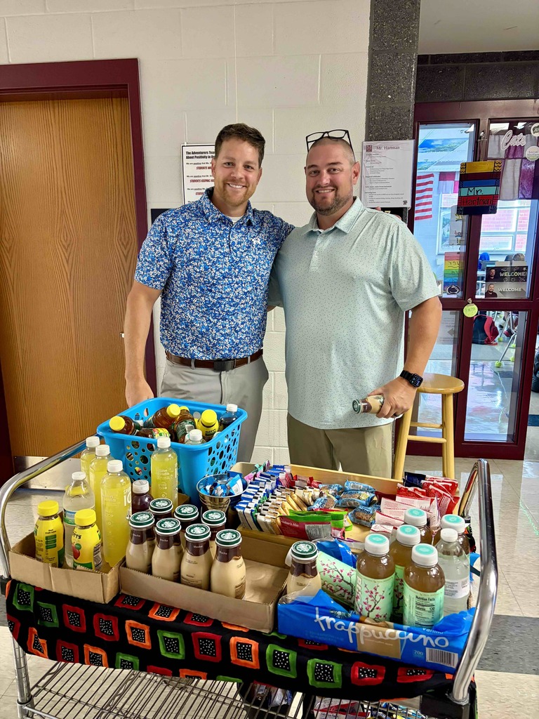 Two men stand behind a snack cart in a school hallway.