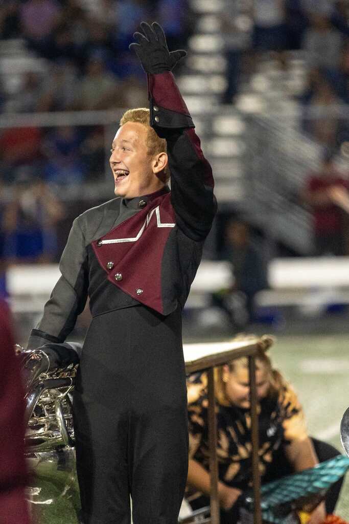 A member of a marching band waves his hand in the air and smiles.