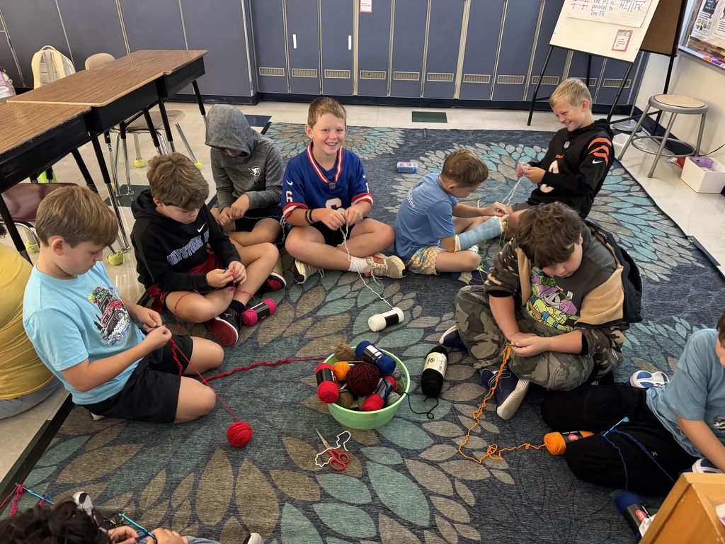 Students sit on a classroom floor as they learn to crochet.