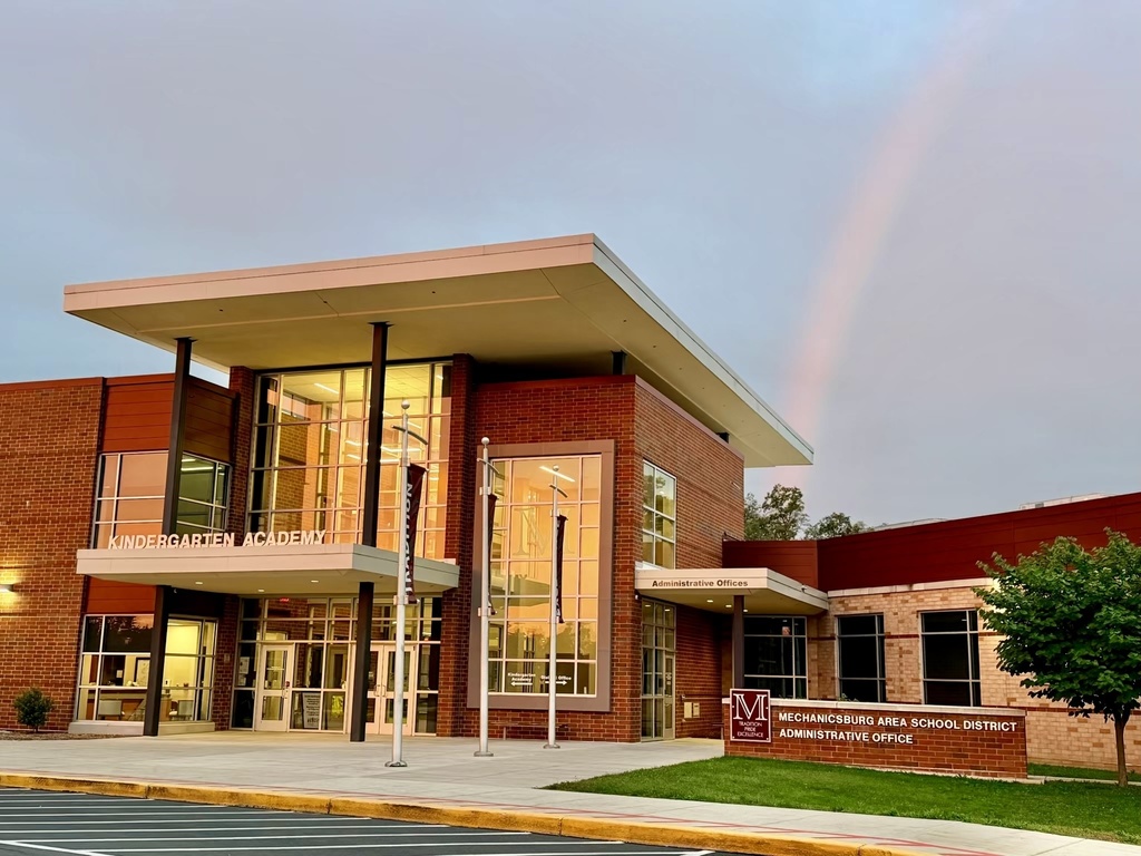 A rainbow over a school building with the sunrise reflecting off the glass windows.