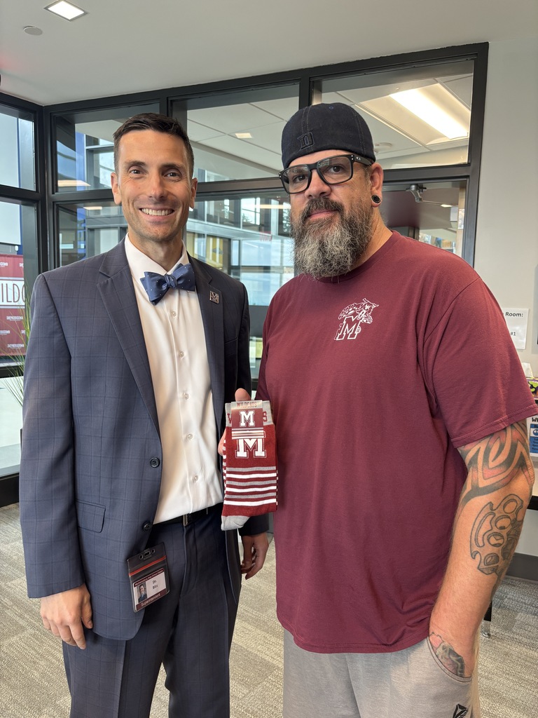 A man in a suit presents a colleague with a pair of maroon, branded socks.