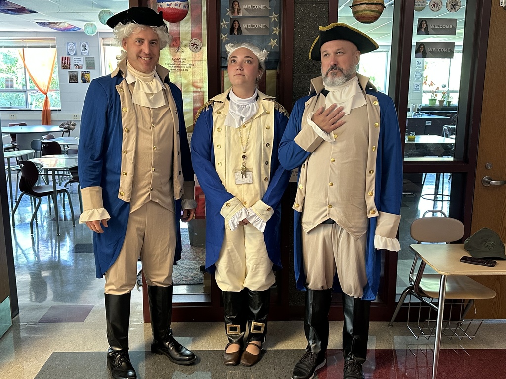 Three teachers dress as George Washington and stand outside a classroom.