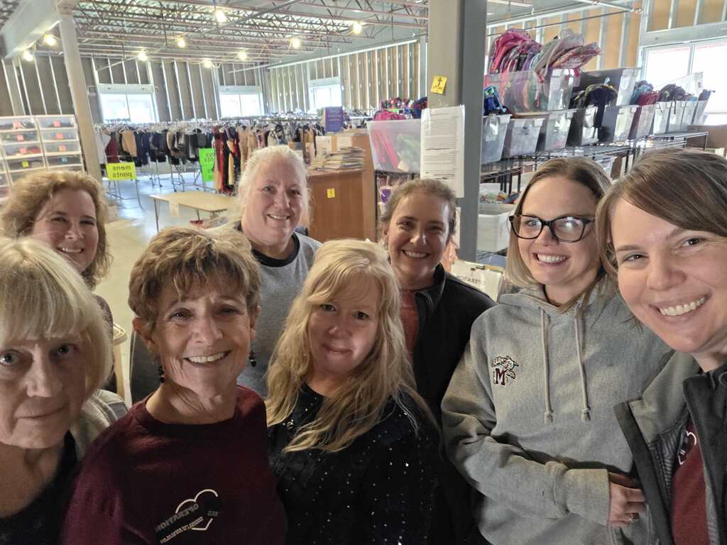 A group of ladies take a selfie in front of a fundraiser yard sale that is being set up.