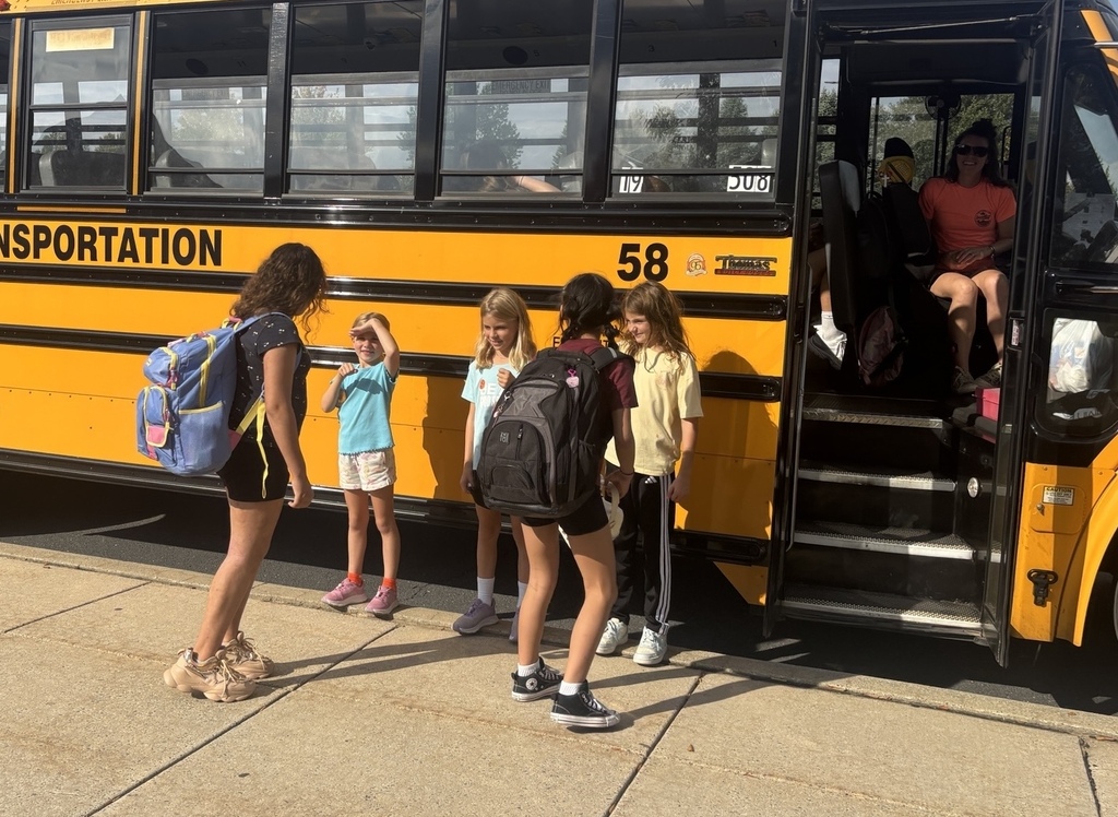 Three elementary students give fist bumps to middle school students on their way to the school bus.