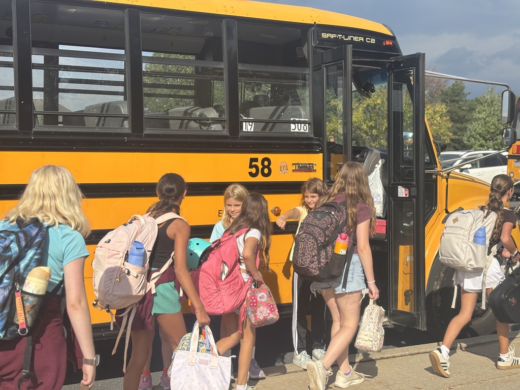 Three elementary students give fist bumps to middle school students on their way to the school bus.