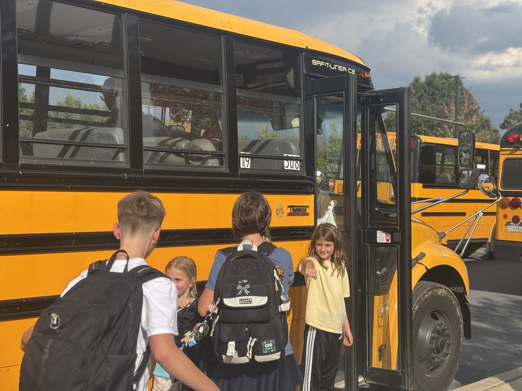 Three elementary students give fist bumps to middle school students on their way to the school bus.