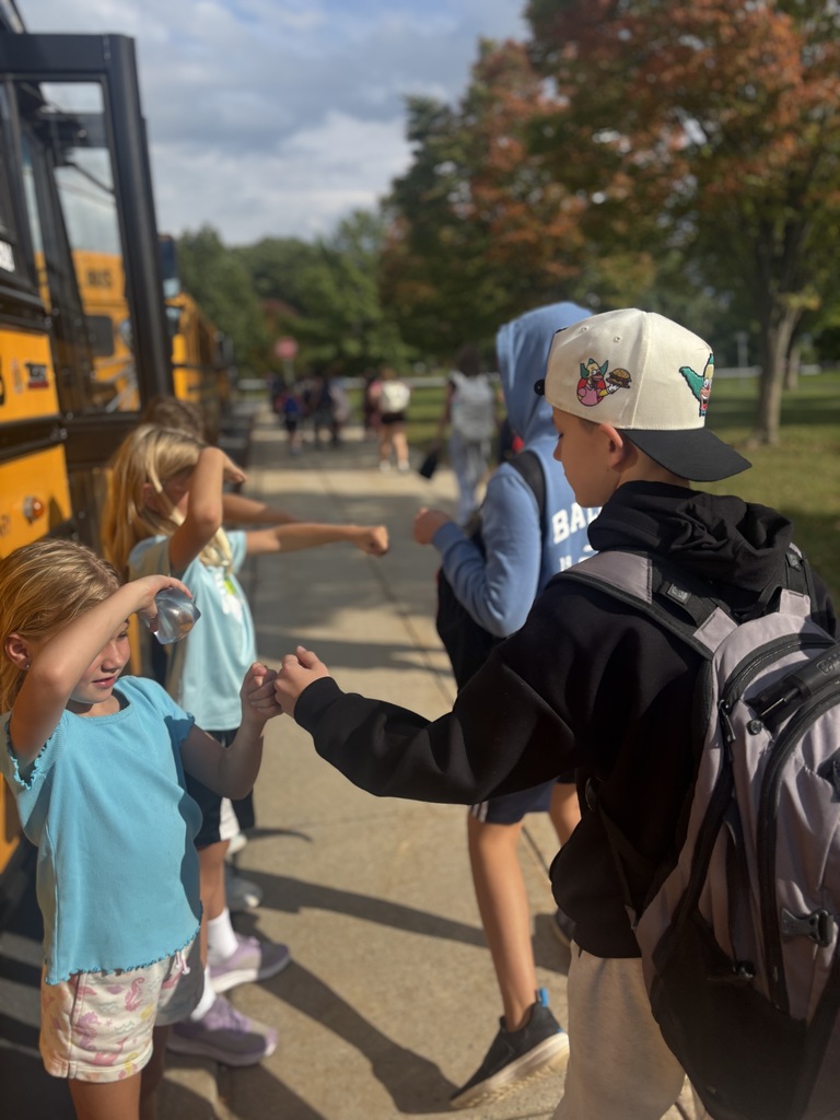 Three elementary students give fist bumps to middle school students on their way to the school bus.