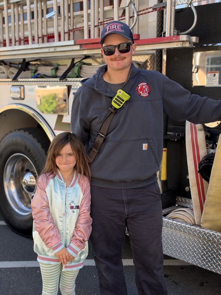 A young student poses for a picture with a firefighter.