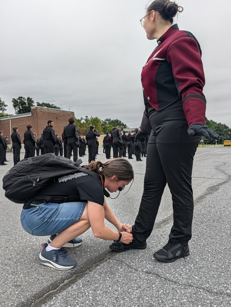 A lady kneels to tie a band member's shoe right before a performance.