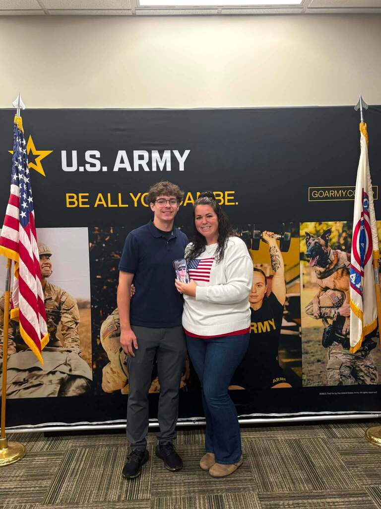 A student poses in front of a US Army banner with his mom after officially signing his commitment to the Army.
