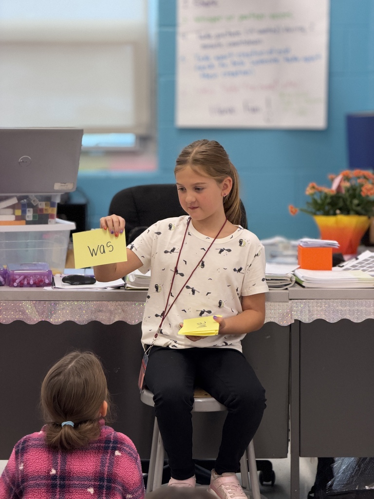 A young student holds up a card with the word "was" written on it as part of a lesson on tricky words.