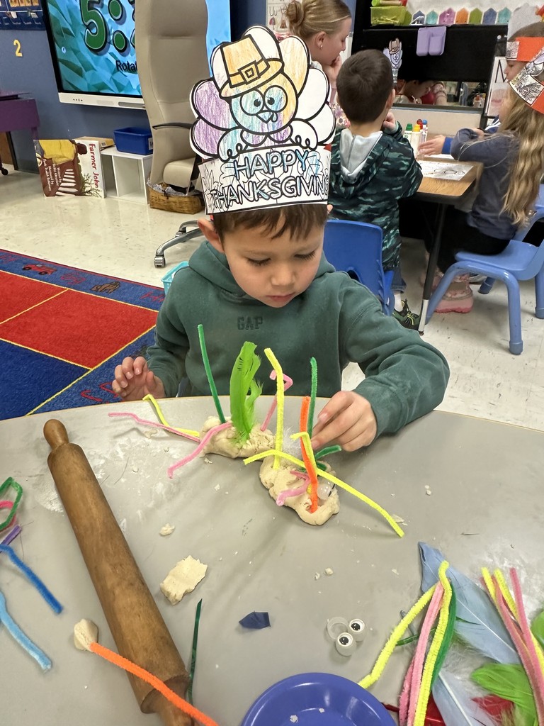 boy in a green shirt with playdough and pipe cleaners and feathers and google feathers