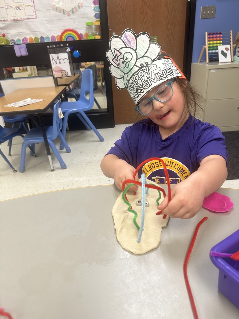girl in a purple shirt with turkey crown playing with playdough