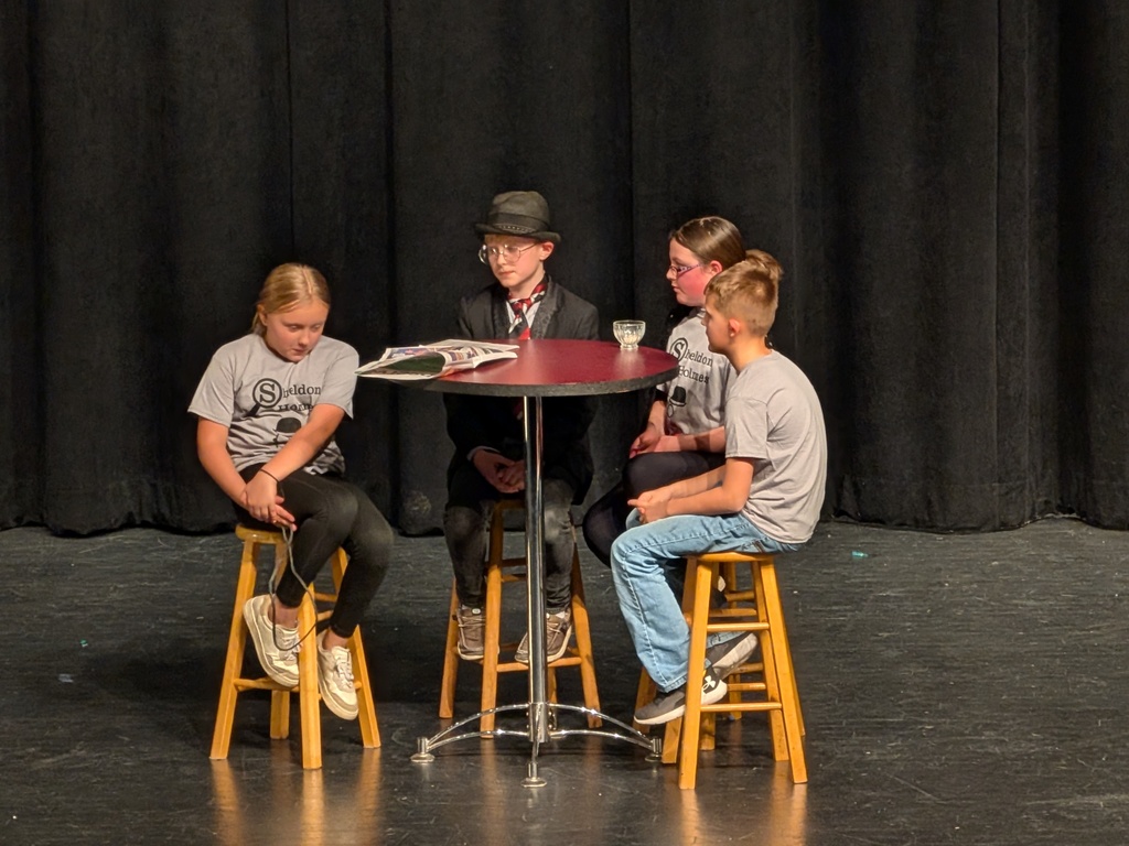 4 kids sitting at a table one wearing a heat and classes