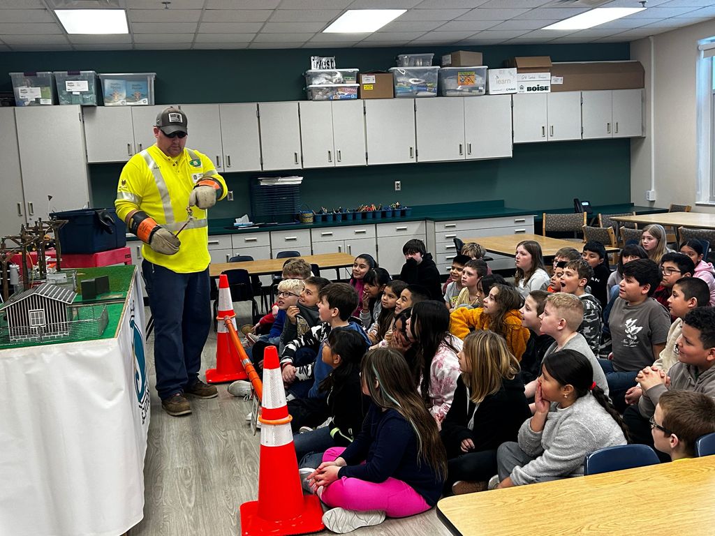 man wearing yellow shirt doing a demonstration in front school kids sitting on the floor.