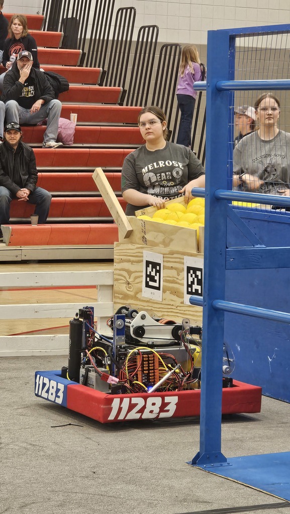 Girl standing by a bin of balls with a robot in front of them