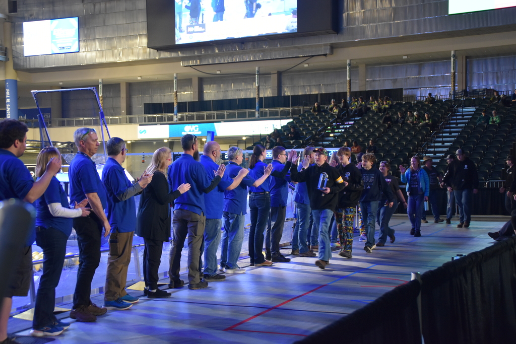 row people with blue shirts high fiving the kids in black shirts