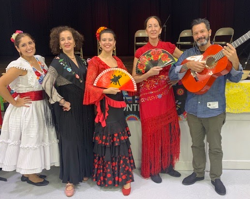 Five adults dressed in traditional clothing pose for a picture with musical instruments on a stage.