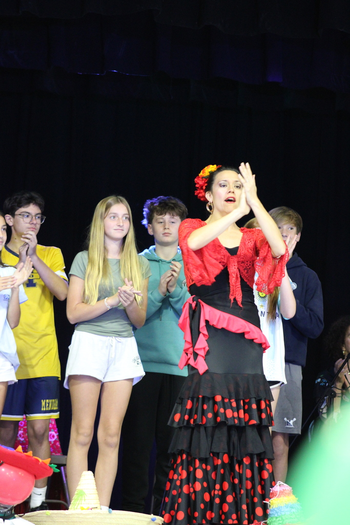 Woman in a black and red dress with flowers in her hair dancing on stage.