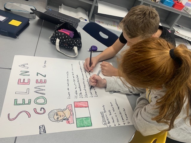 Two children writing on a poster with a drawing of a woman and the words "Selena Gomez".