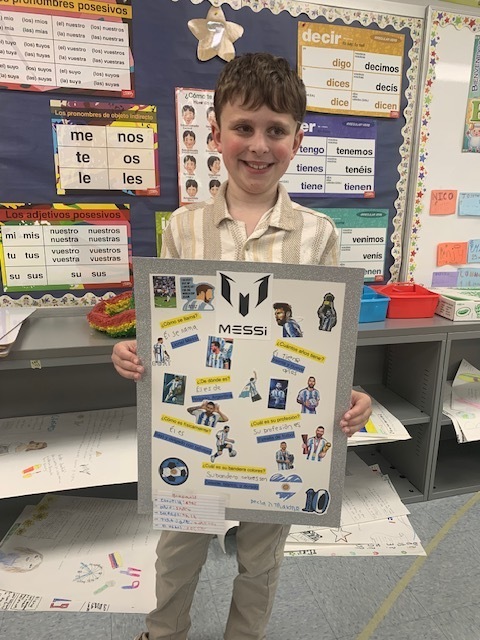 A boy holds a framed poster featuring various photos of soccer players and a few words.