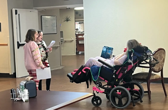 The photo shows the Pacific Intermediate JAG Club and 5th grade choir students spreading holiday cheer at the Pacific Care Center