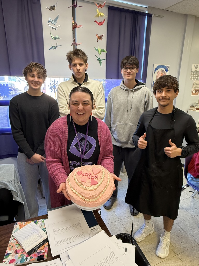 High school students holding a pink decorated cake with staff member.