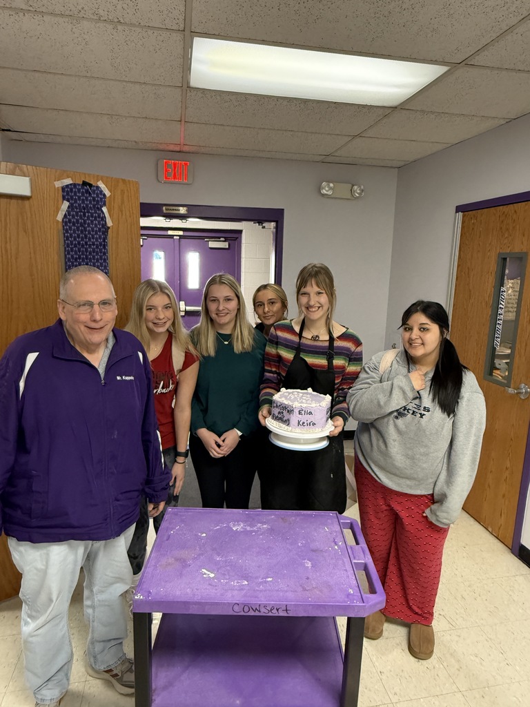 High school students holding a purple decorated cake with staff member.