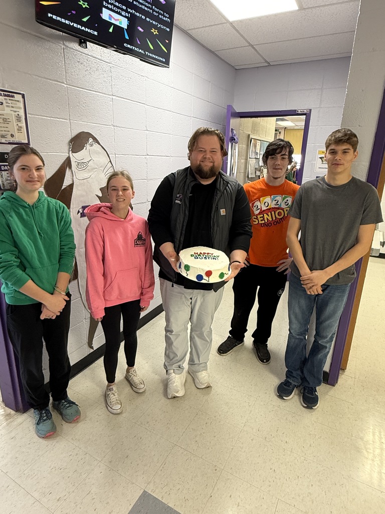 High school students holding a happy birthday decorated cake with staff member.