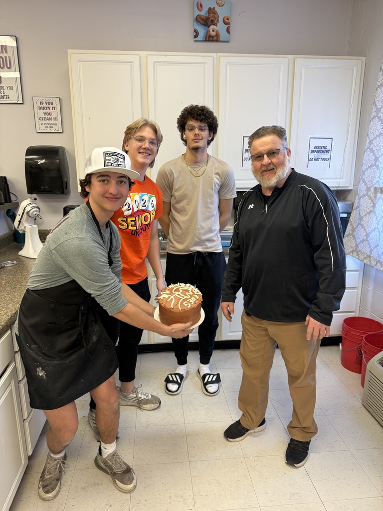 High school students holding a brown decorated cake with staff member.