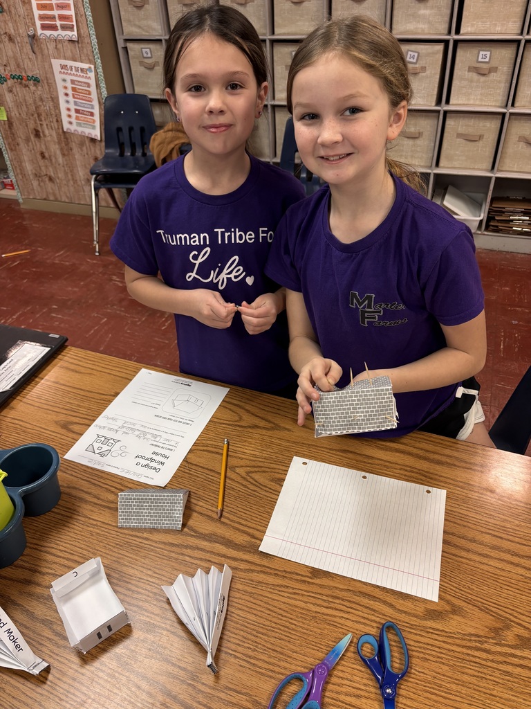 Two young students making a paper house smiling. 