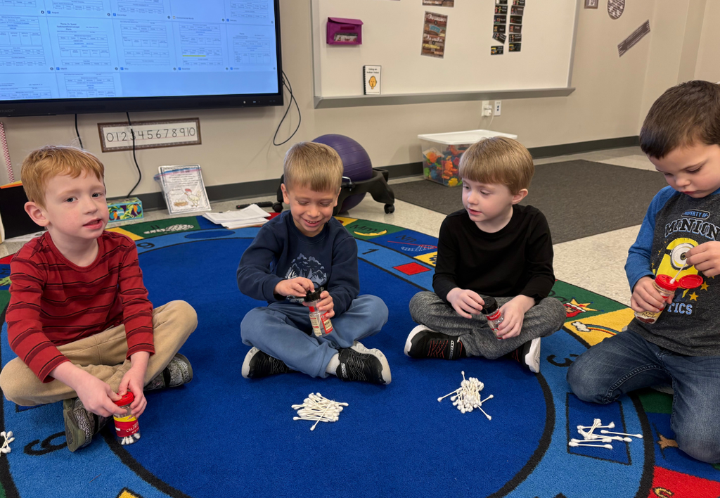 Four young students doing an activity with q-tips on a blue rug.