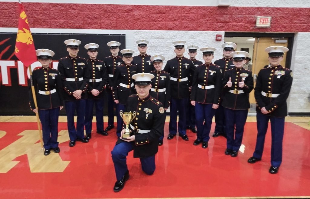 Drill team group photo with their trophy in a red gym.