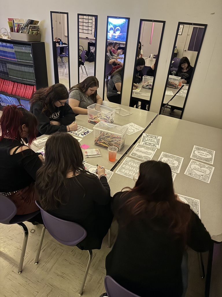 Group of students sitting at a large desk coloring on coloring pages.