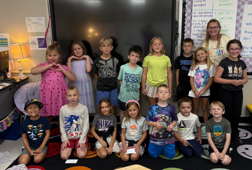 Group of elementary students posing with their teacher in a classroom.