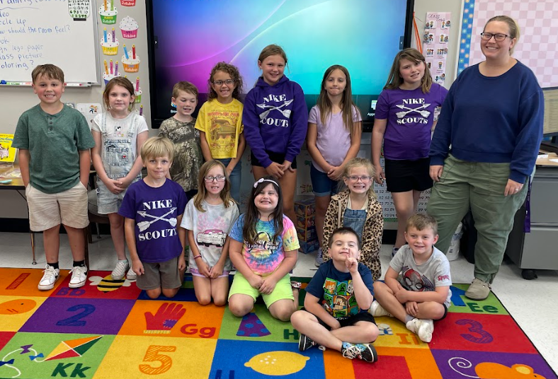 Group of elementary students posing with their teacher in a classroom.